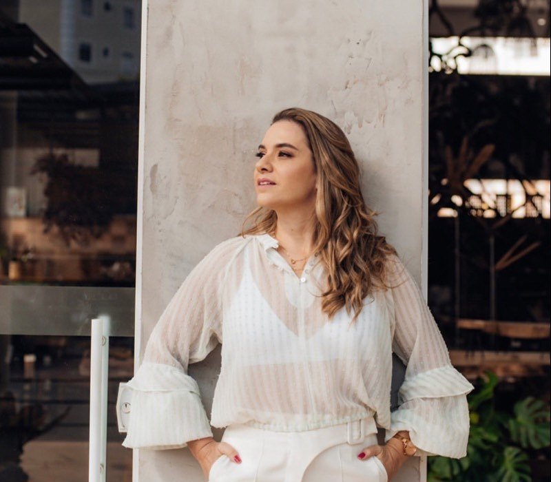 Dra. Laura Nalon de blusa branca, encostada em uma coluna de concreto